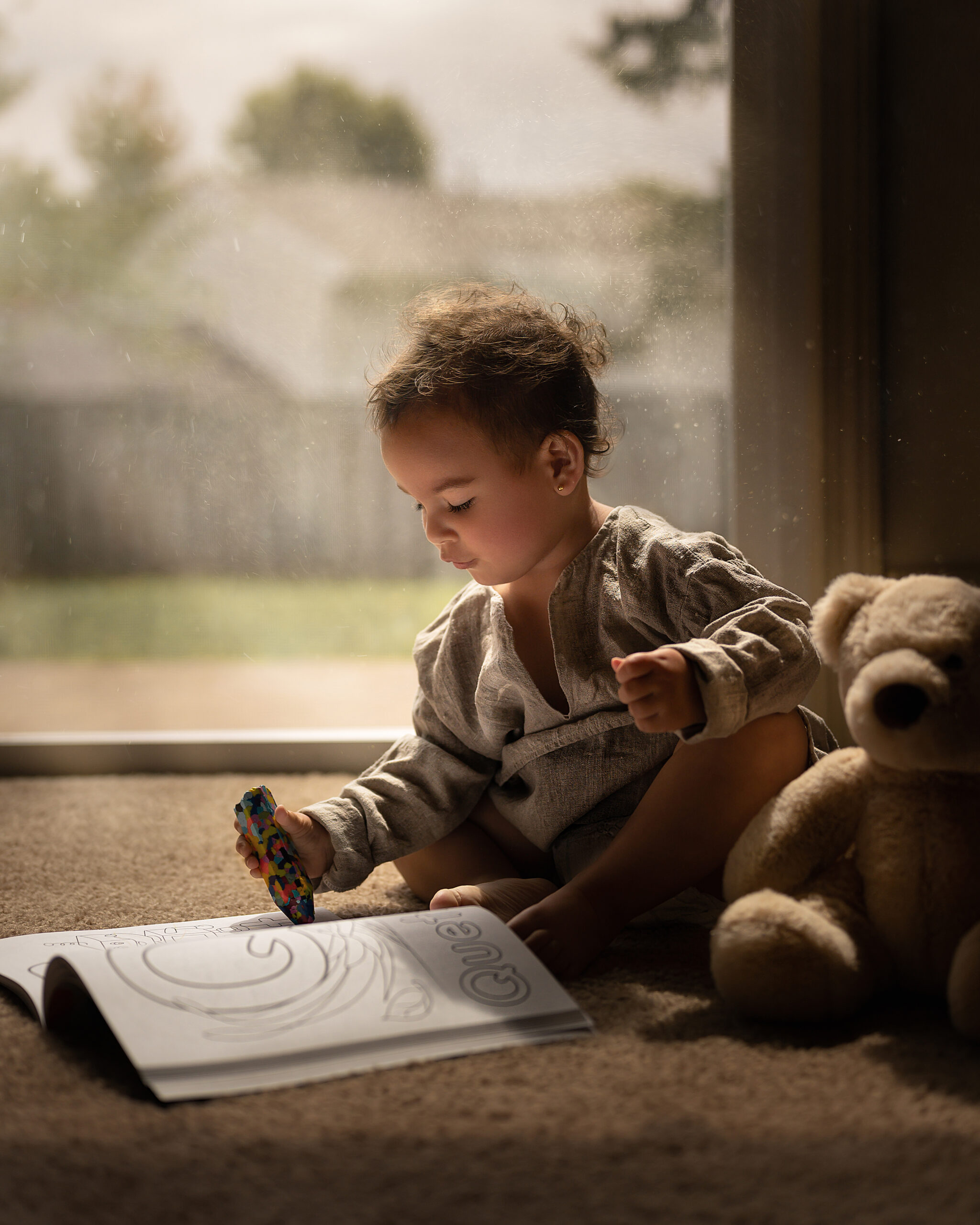 child coloring on the floor with a teddy bear